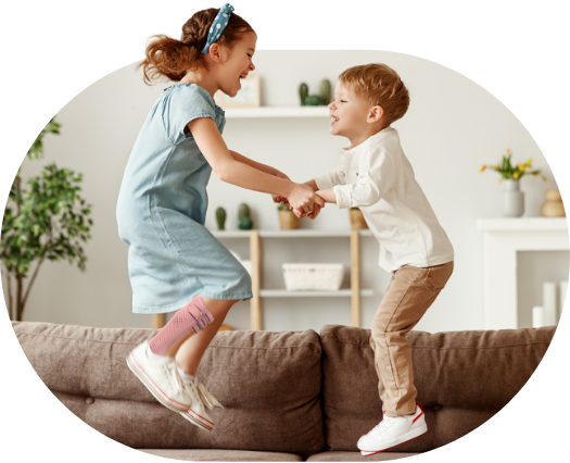 two children jumping on sofa holding hands, one child wearing piro, an afo brace